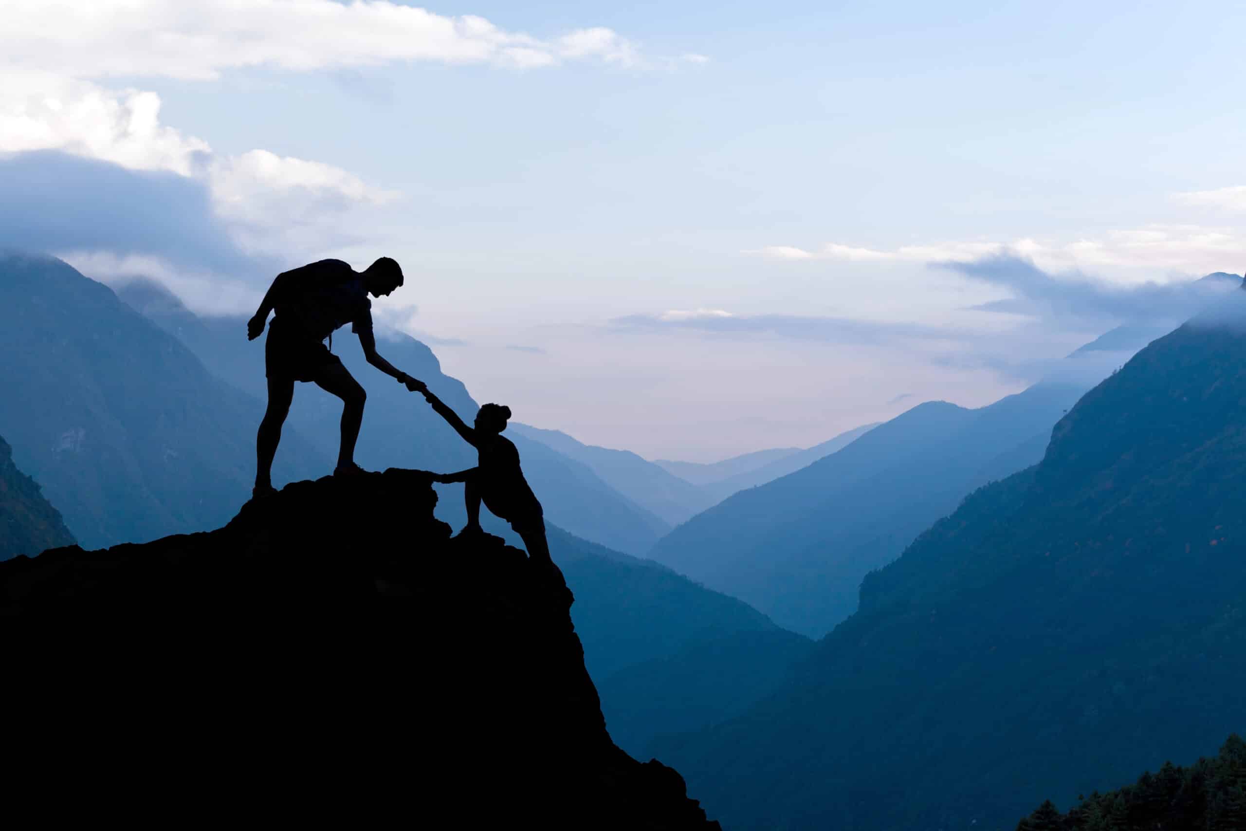 Two people helping each other climb a mountain